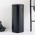 Black trash bin on a white floor with a white wall background